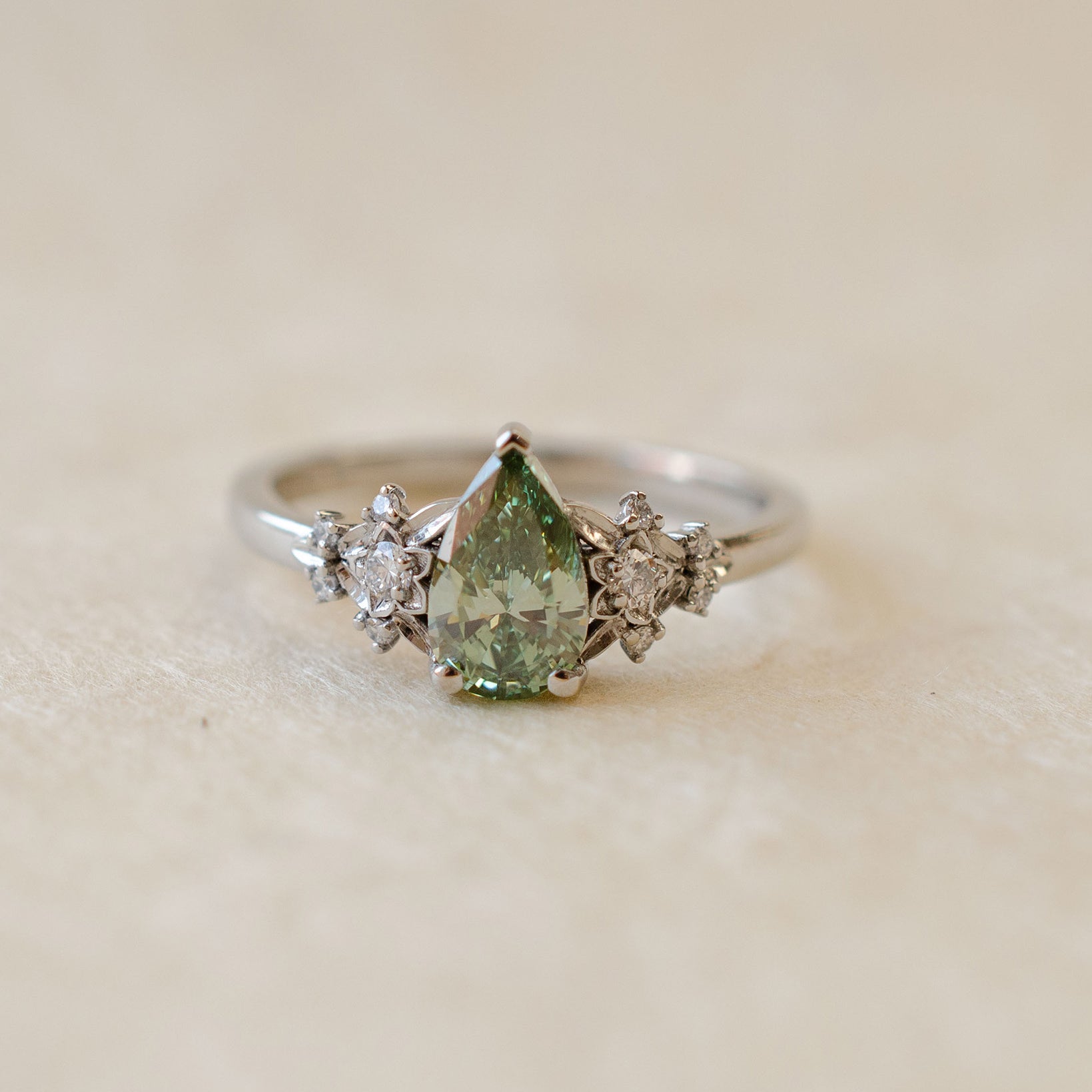 Silver ring with a green gemstone and smaller diamonds on a beige background
