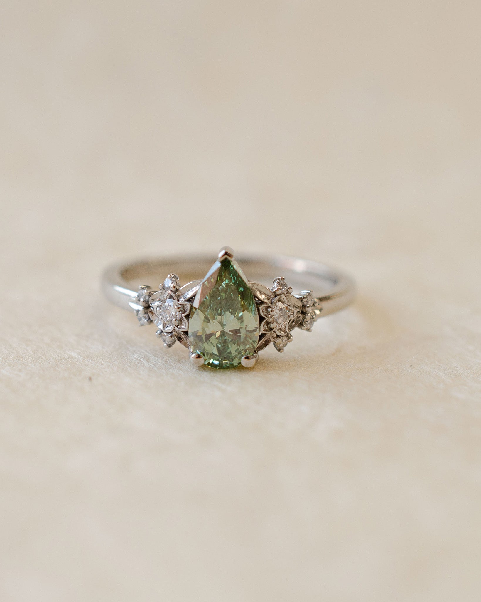 Silver ring with a green gemstone and smaller diamonds on a beige background