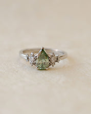 Silver ring with a green gemstone and smaller diamonds on a beige background