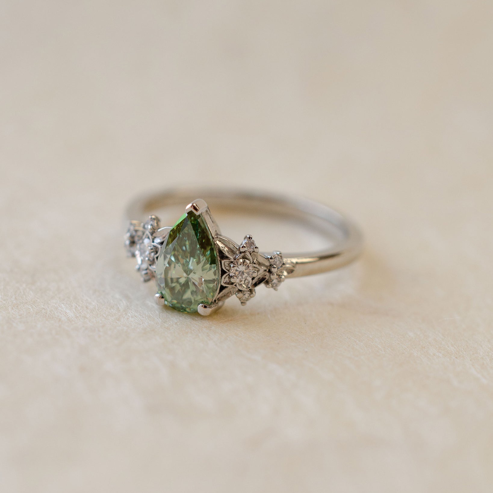 Ring with a green pear-shaped gemstone on a beige background