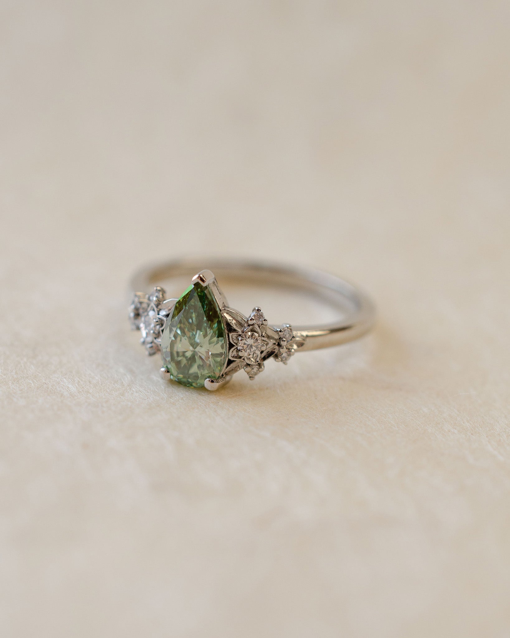 Ring with a green pear-shaped gemstone on a beige background