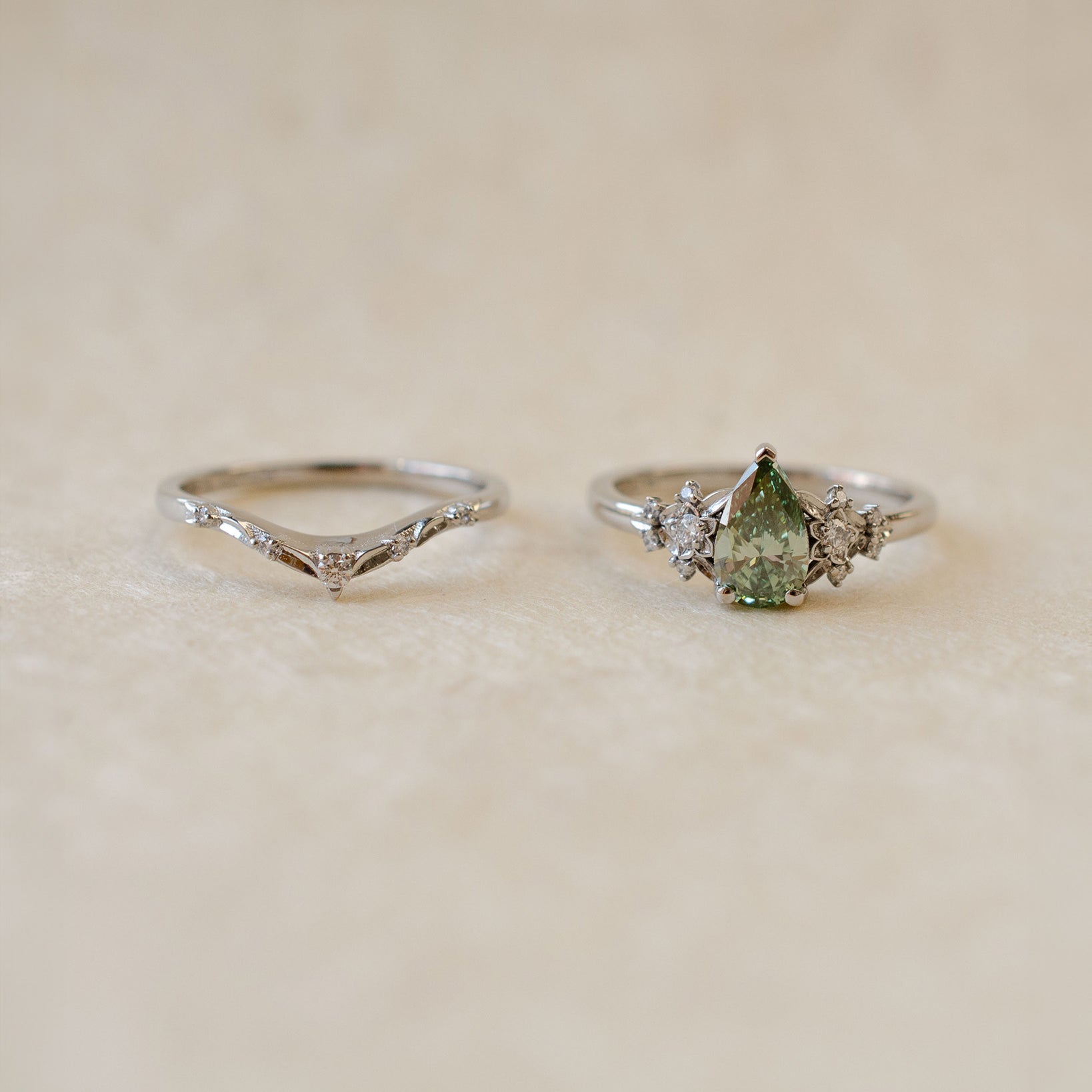 platinum V shaped wedding band next to green diamond engagement ring