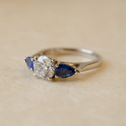 Three-stone ring with a central diamond flanked by two sapphires on a beige background