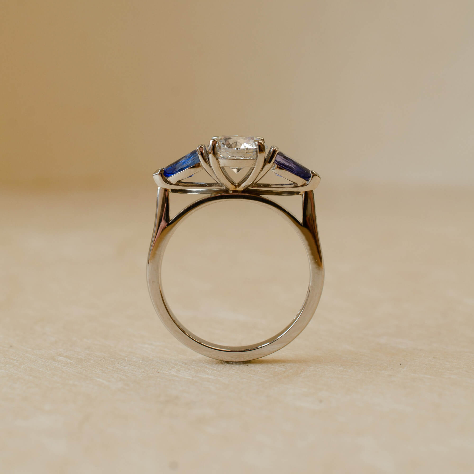 Platinum ring with a central diamond and sapphire stones on a beige background