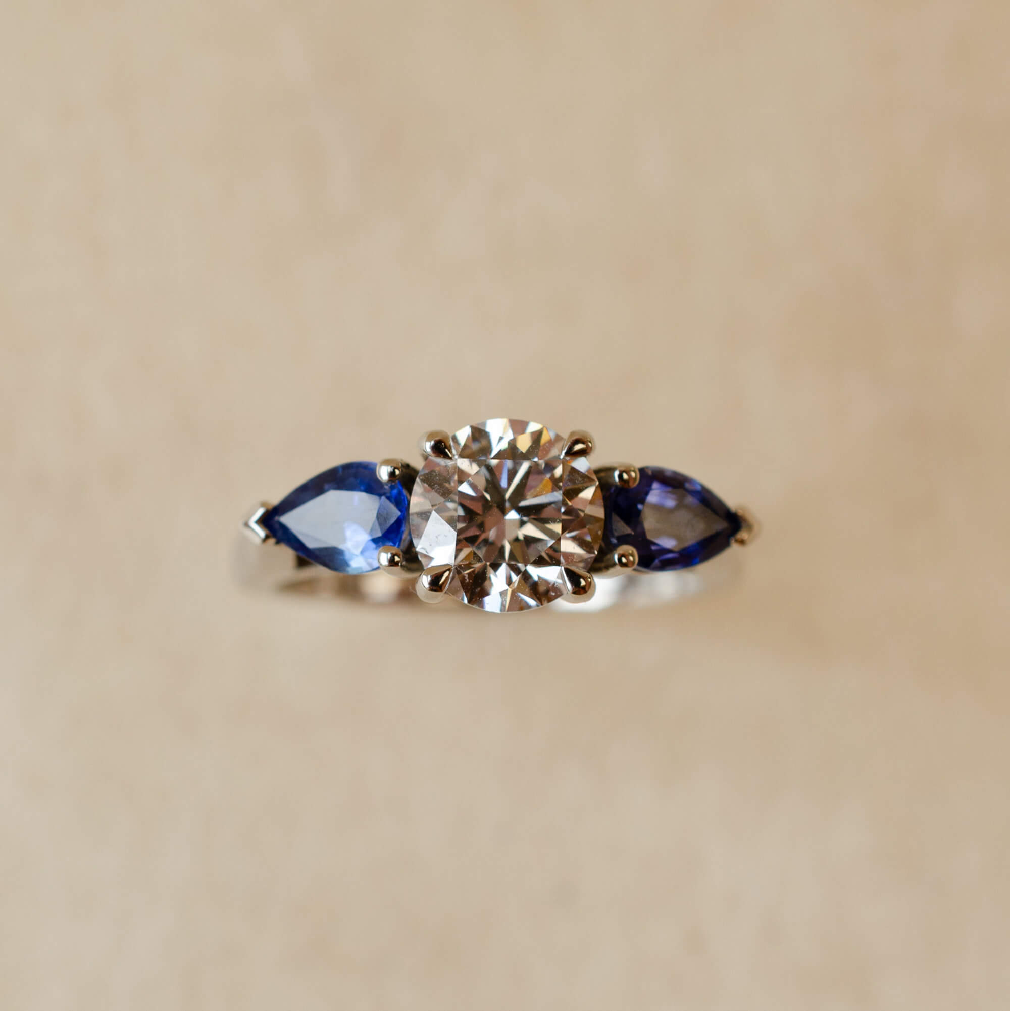 Platinum trilogy ring with round diamond and pear cut blue sapphires