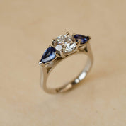 Gold ring with a central diamond and two sapphire stones on a beige background