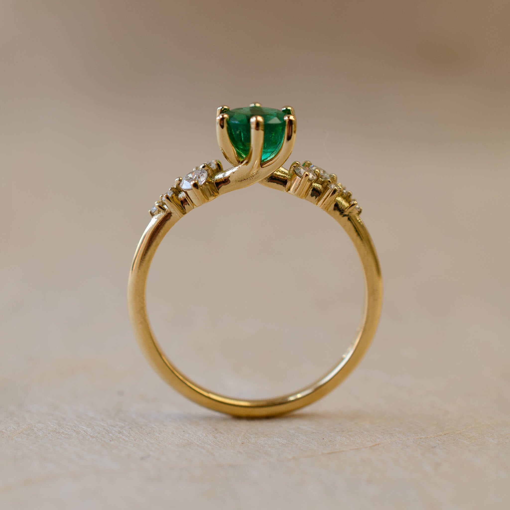 Gold ring with a green gemstone on a beige background