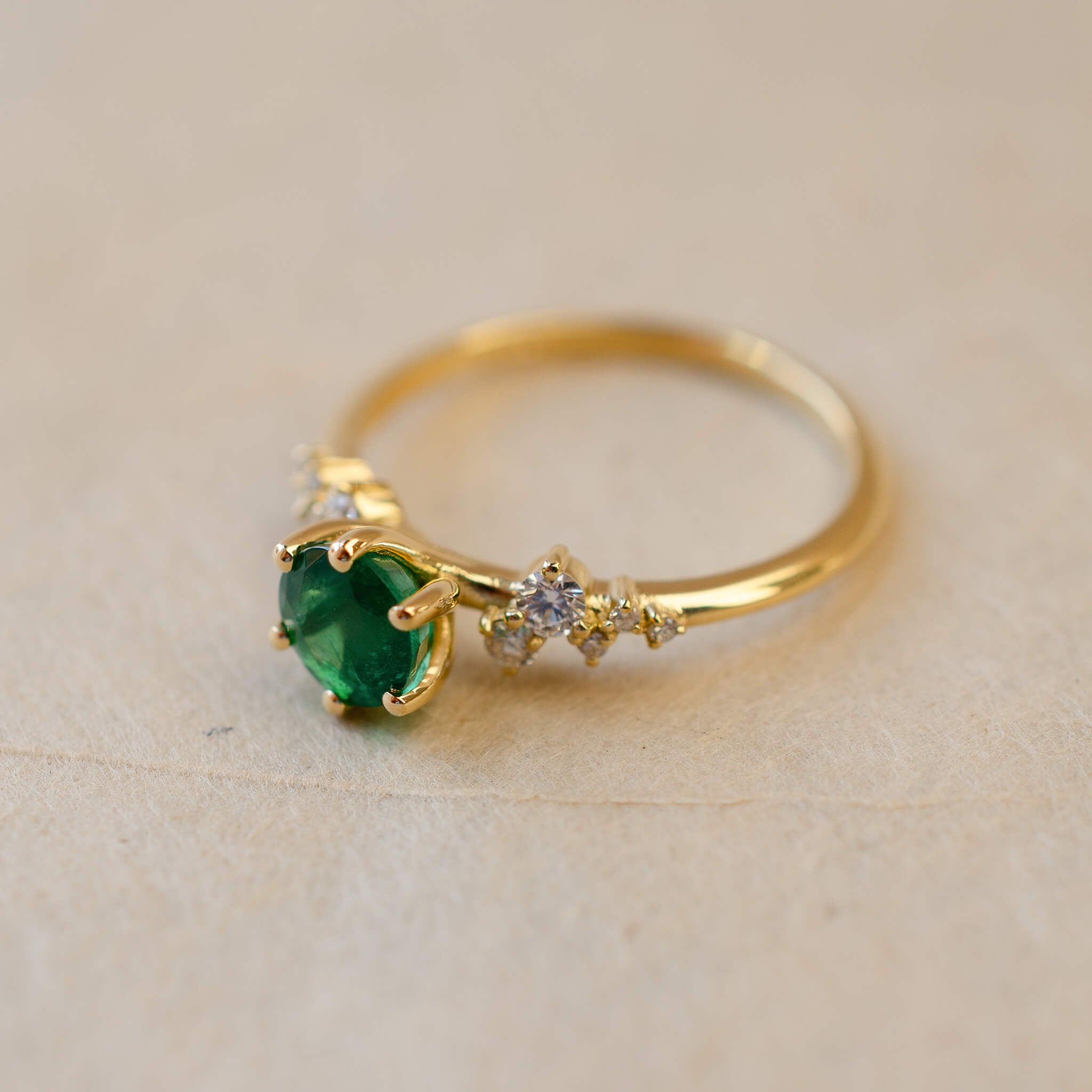 Gold ring with a green gemstone on a beige background