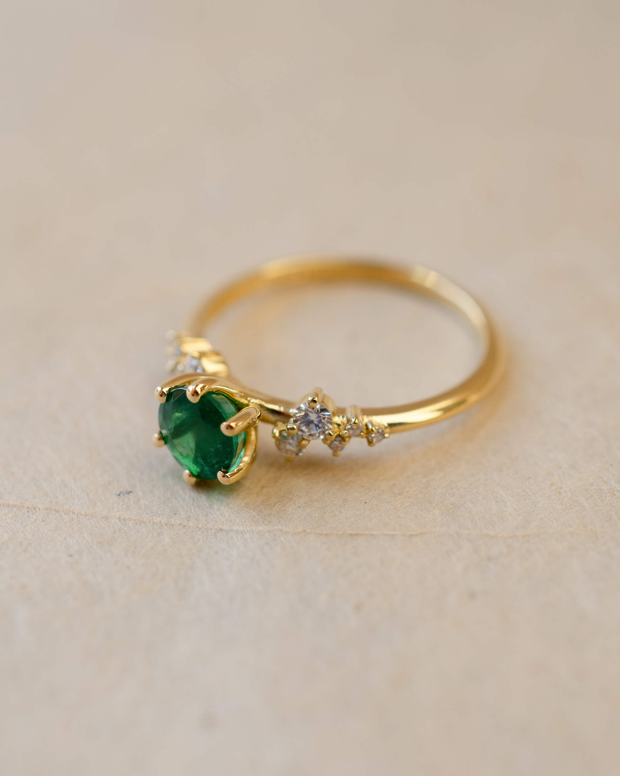 Gold ring with a green gemstone on a beige background