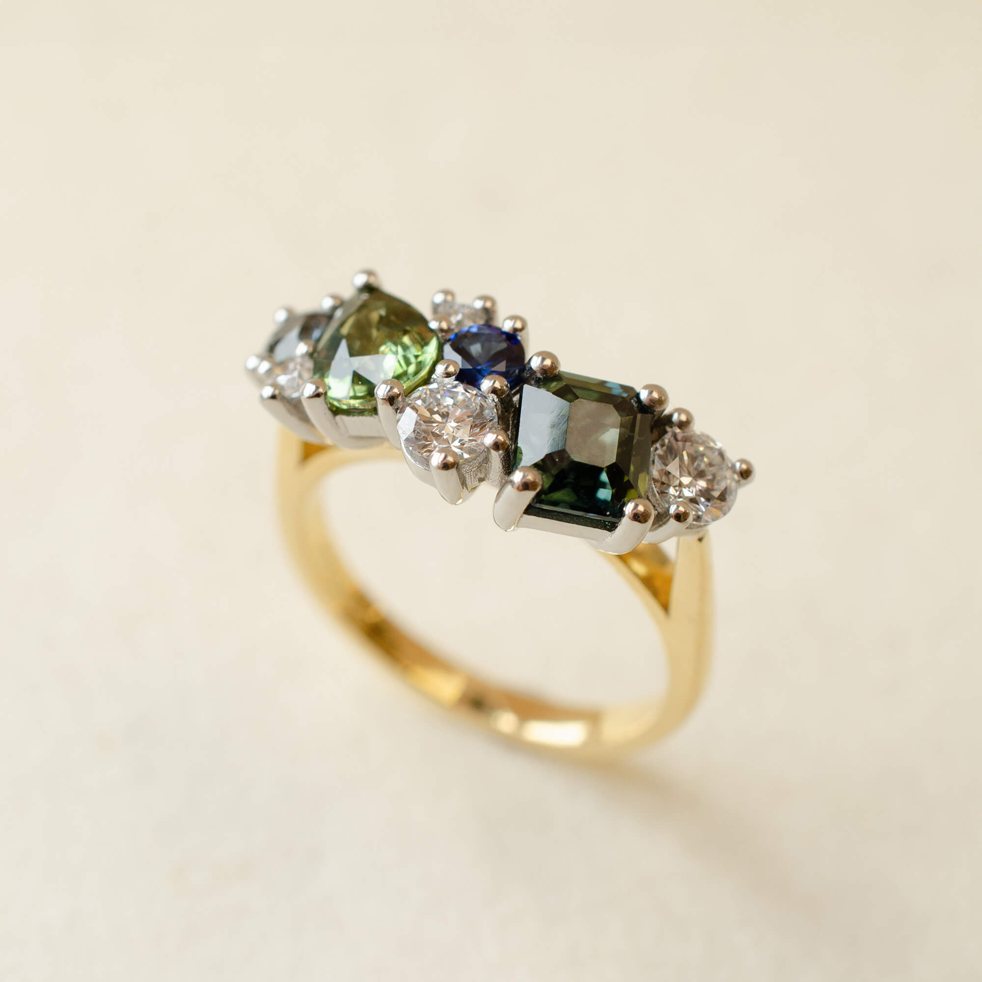 Gold ring with green and blue gemstones on a beige background