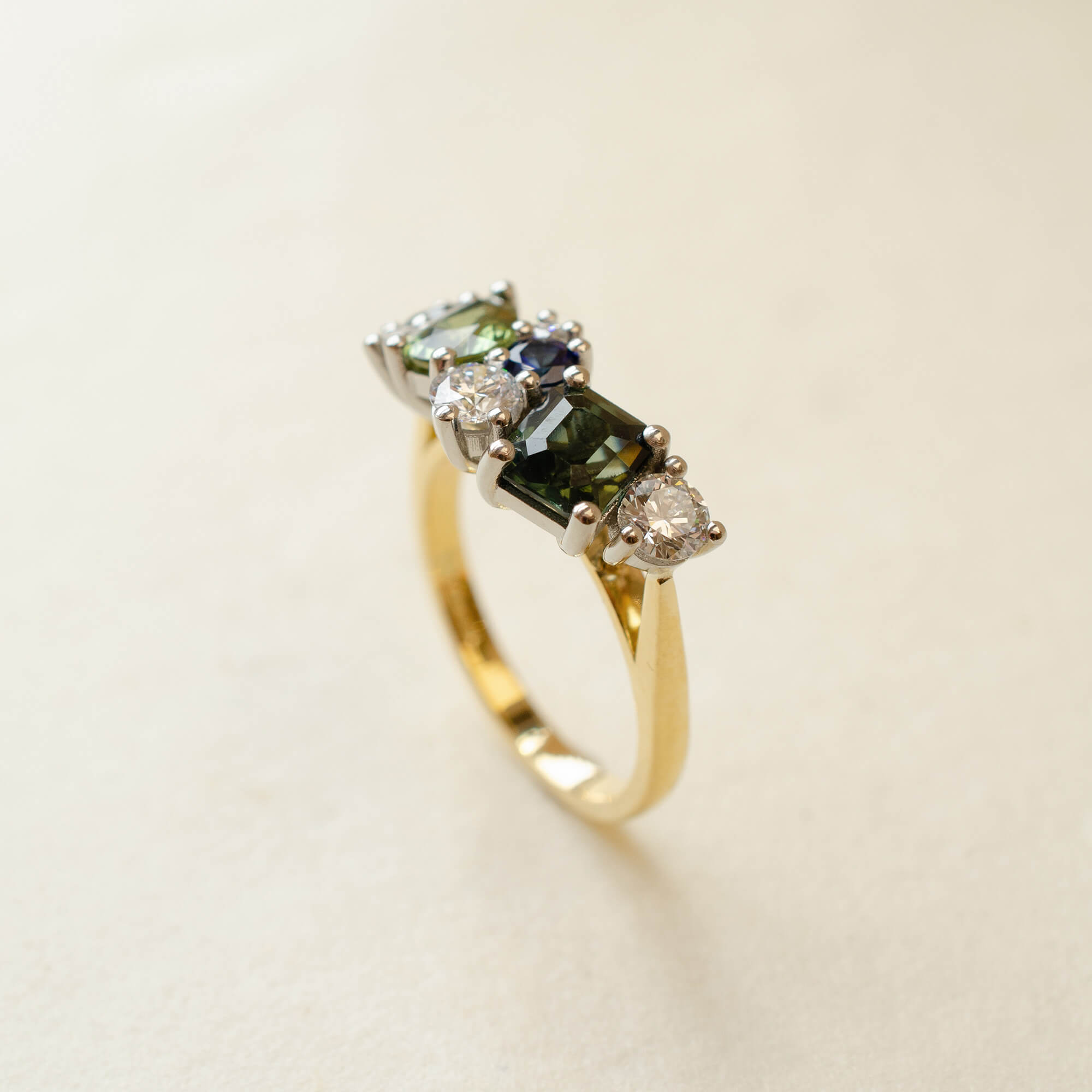 Gold ring with green gemstones on a beige background