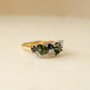 Gold ring with green and blue gemstones on a beige background