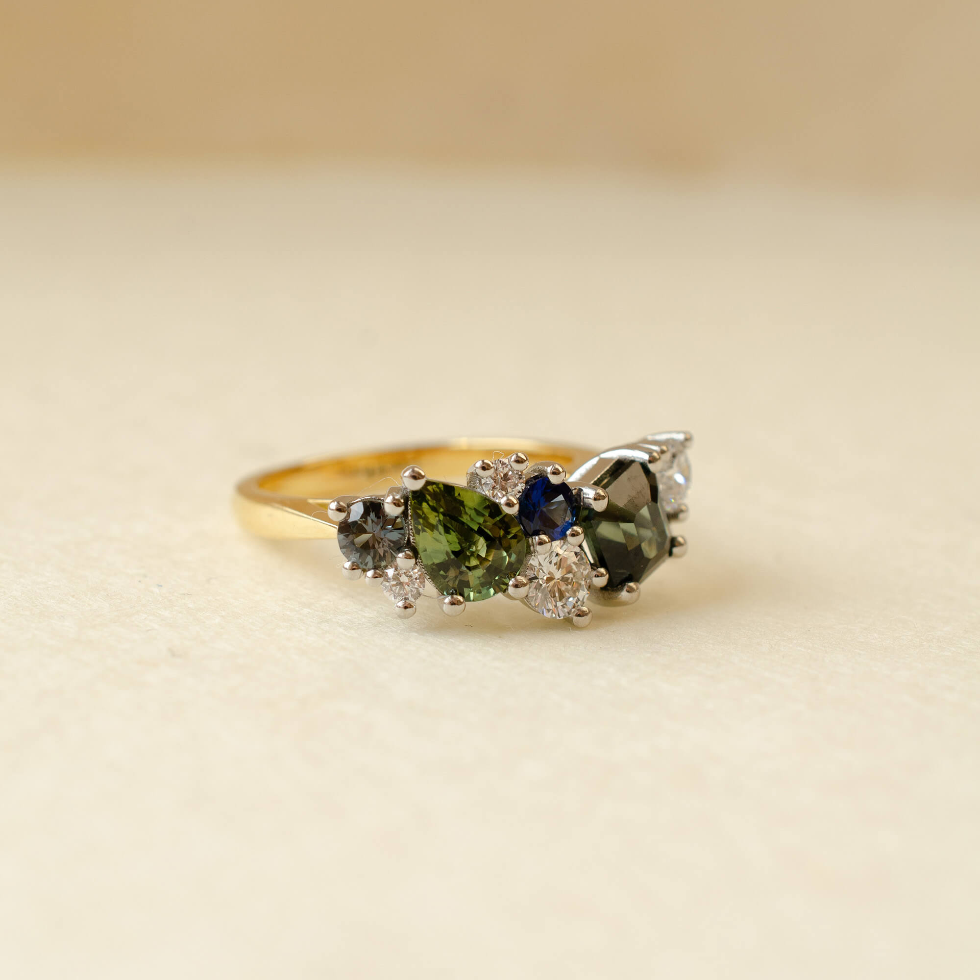 Gold ring with green and blue gemstones on a beige background