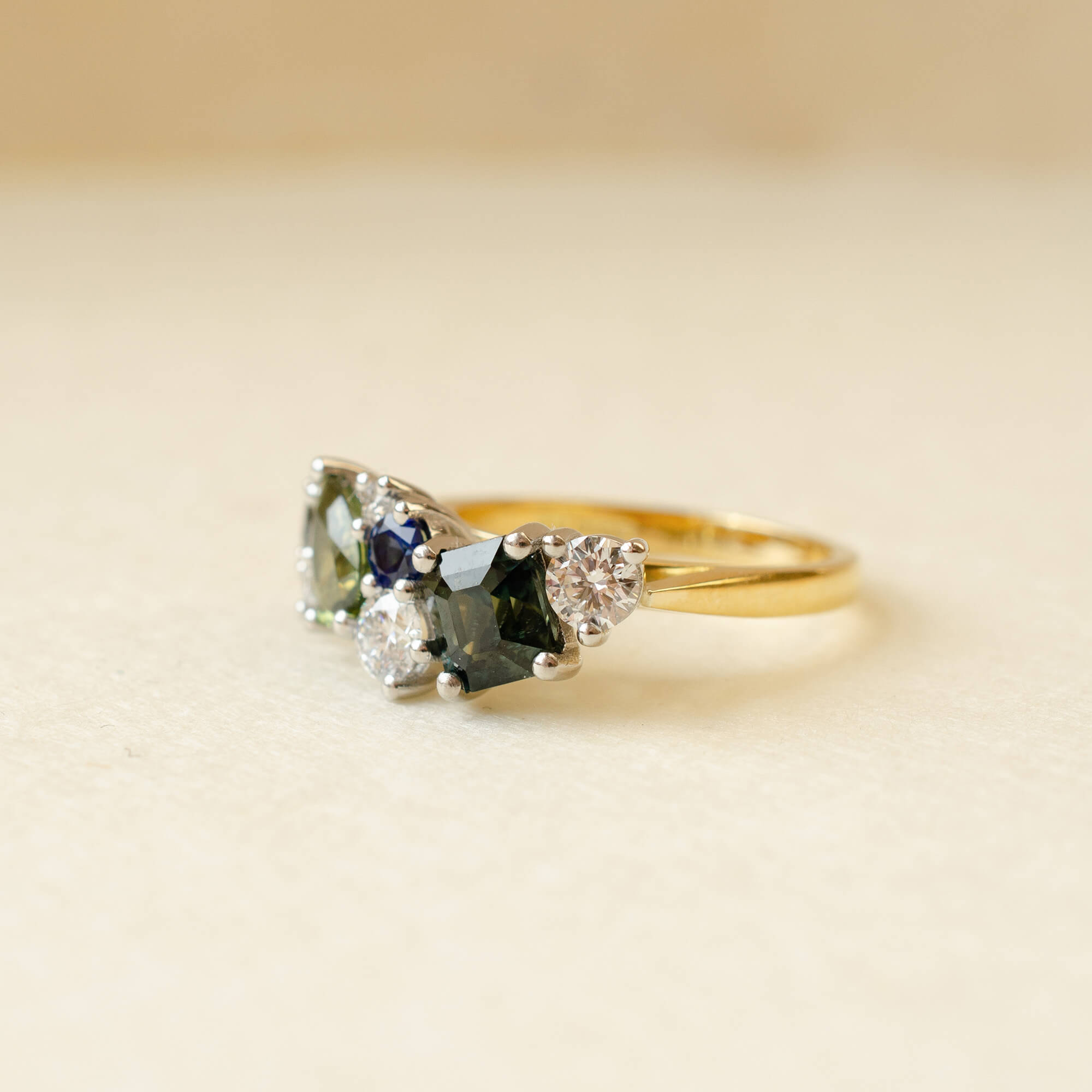 Gold ring with green and blue gemstones on a beige background