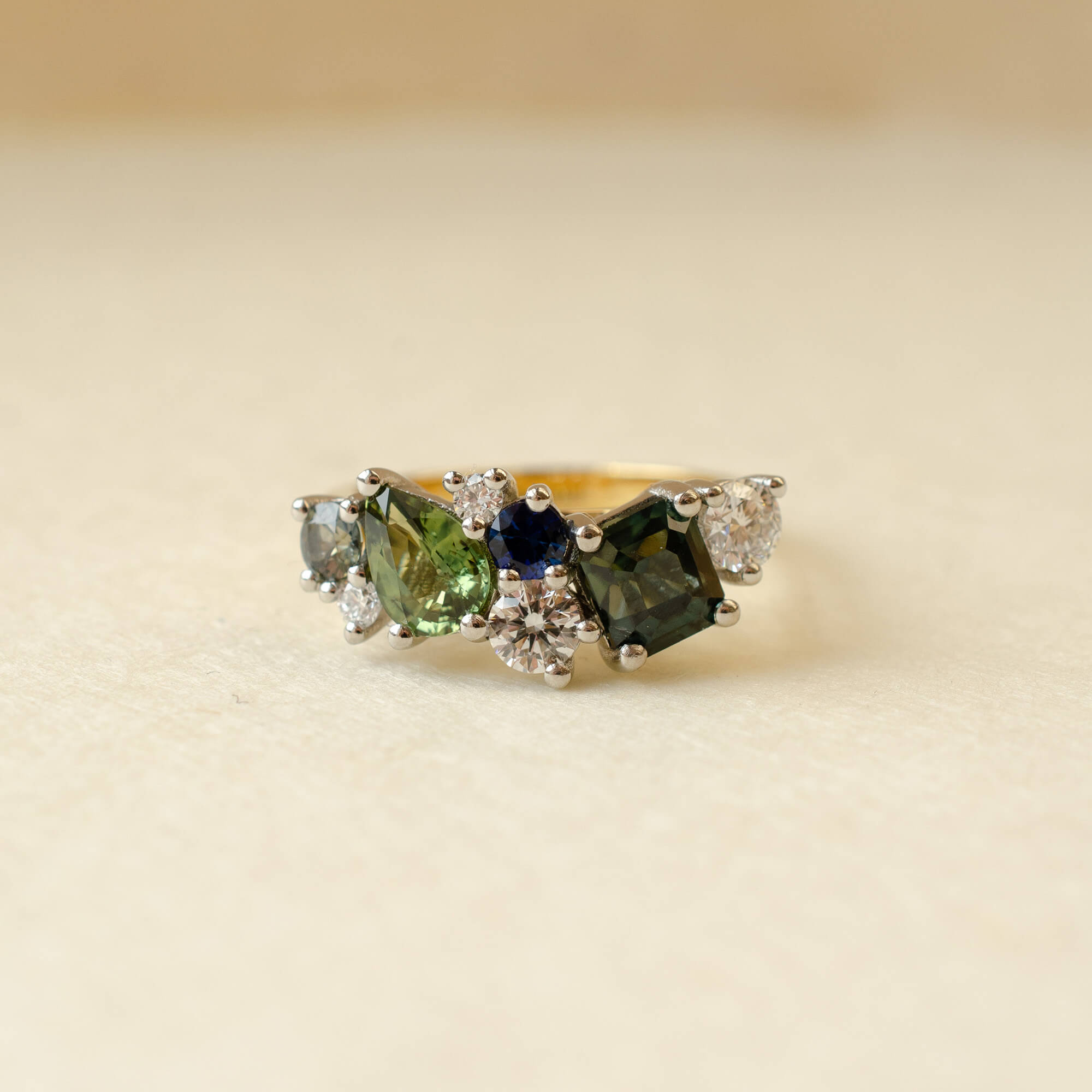 Ring with green gemstones and diamonds on a beige background