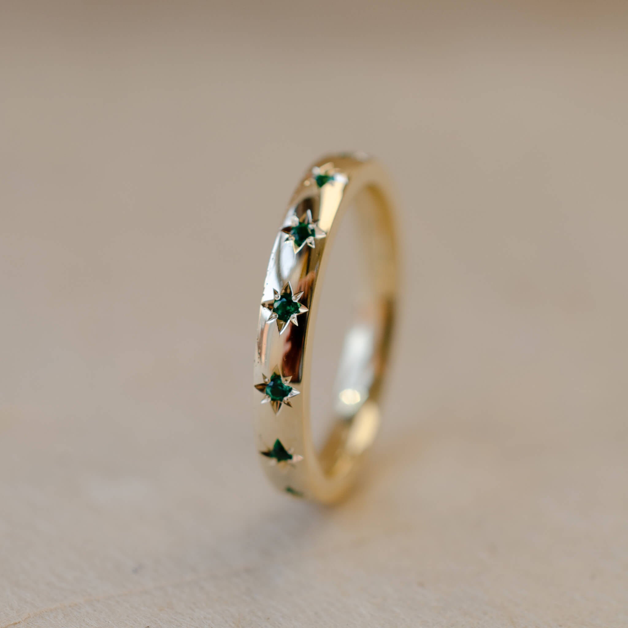 Gold ring with green gemstones on a beige background