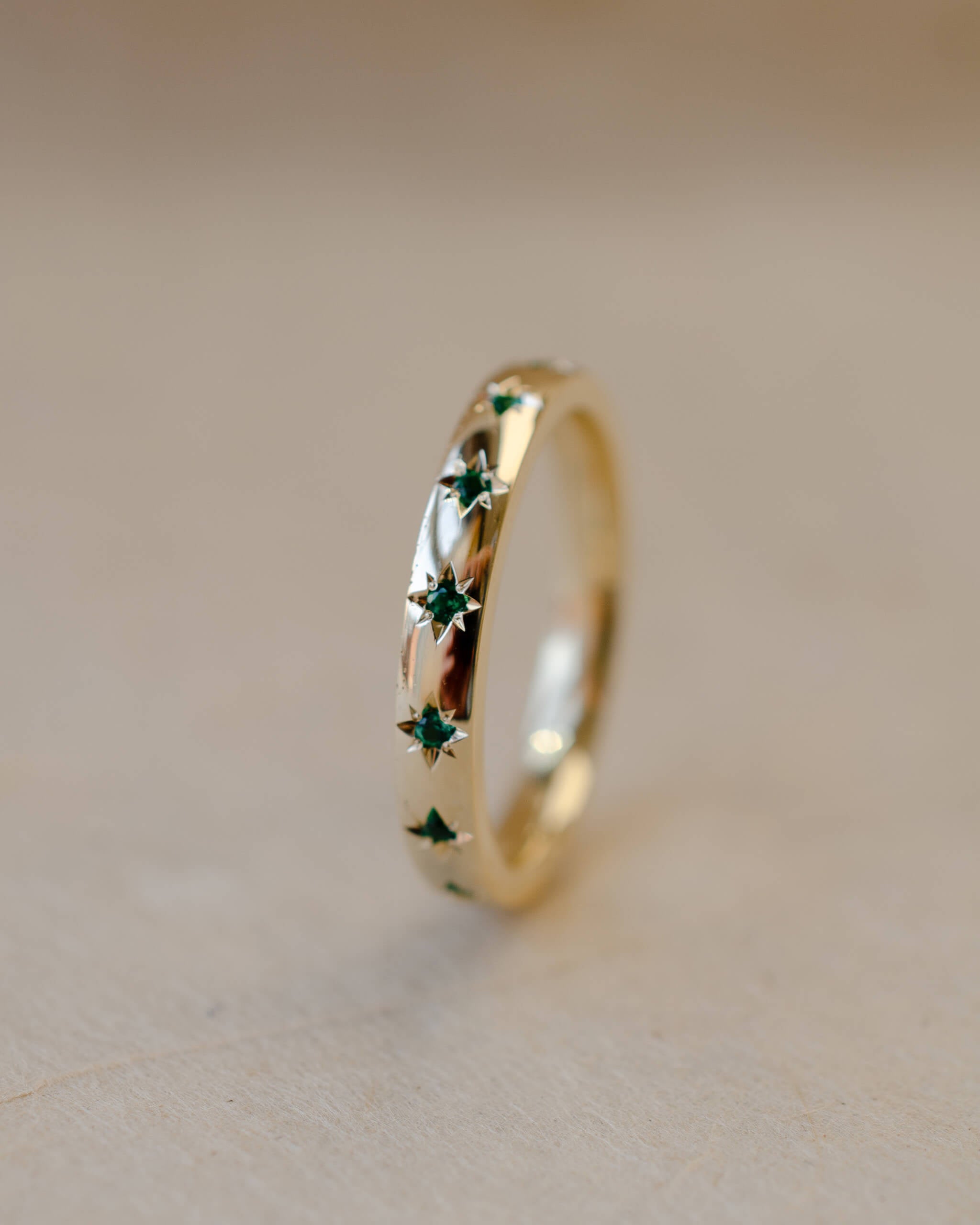 Gold ring with green gemstones on a beige background