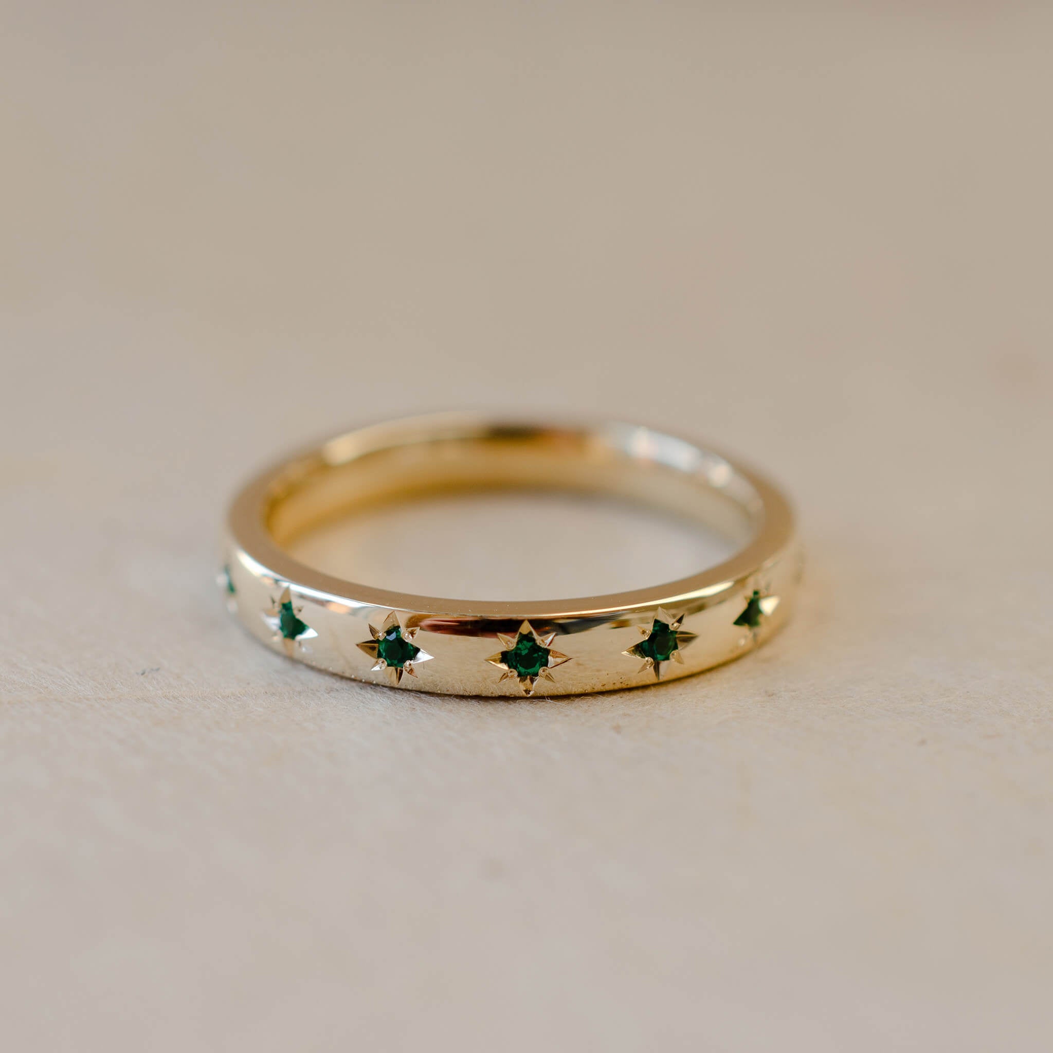 Gold ring with green gemstones on a beige background