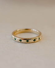 Gold ring with green gemstones on a beige background