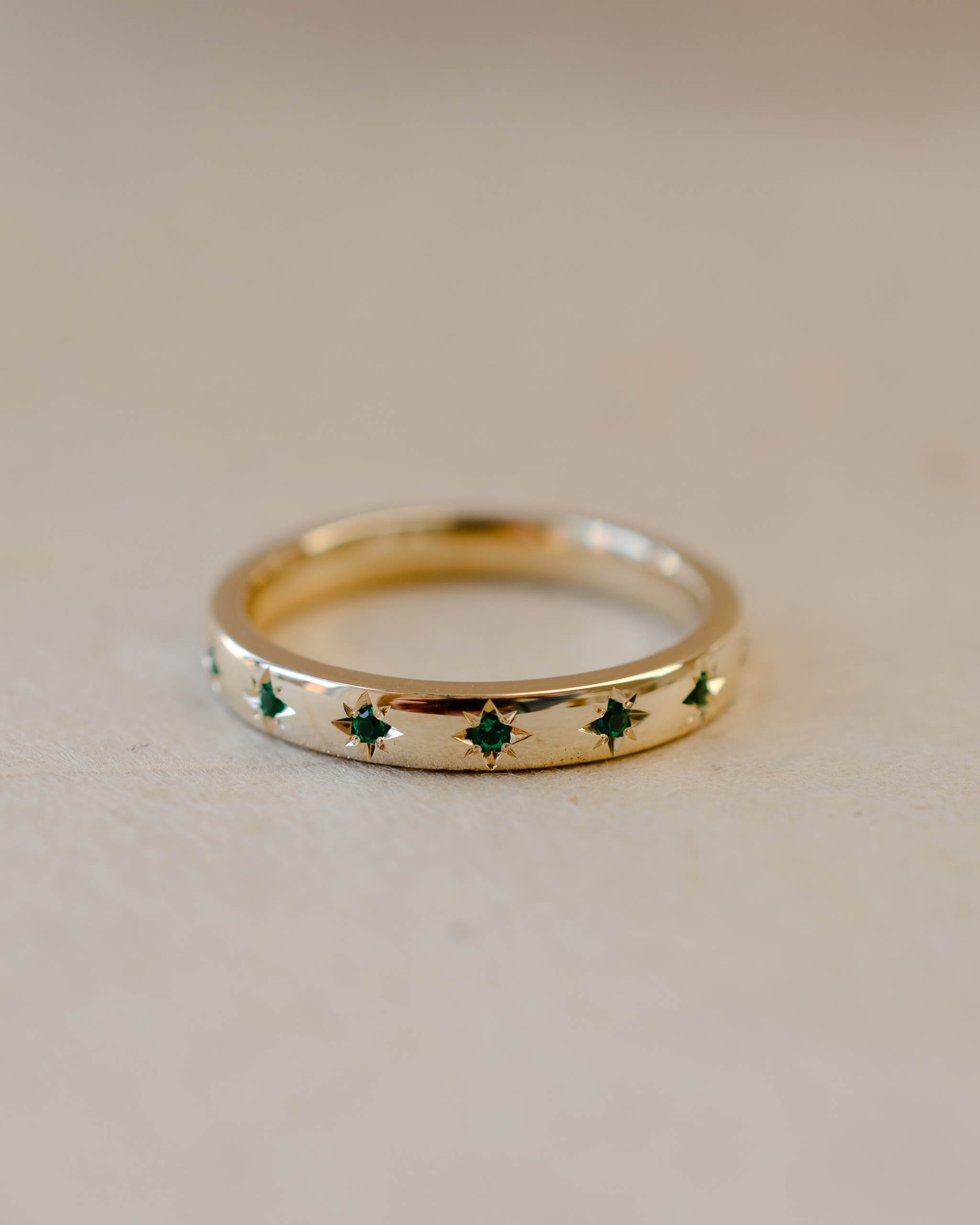 Gold ring with green gemstones on a beige background