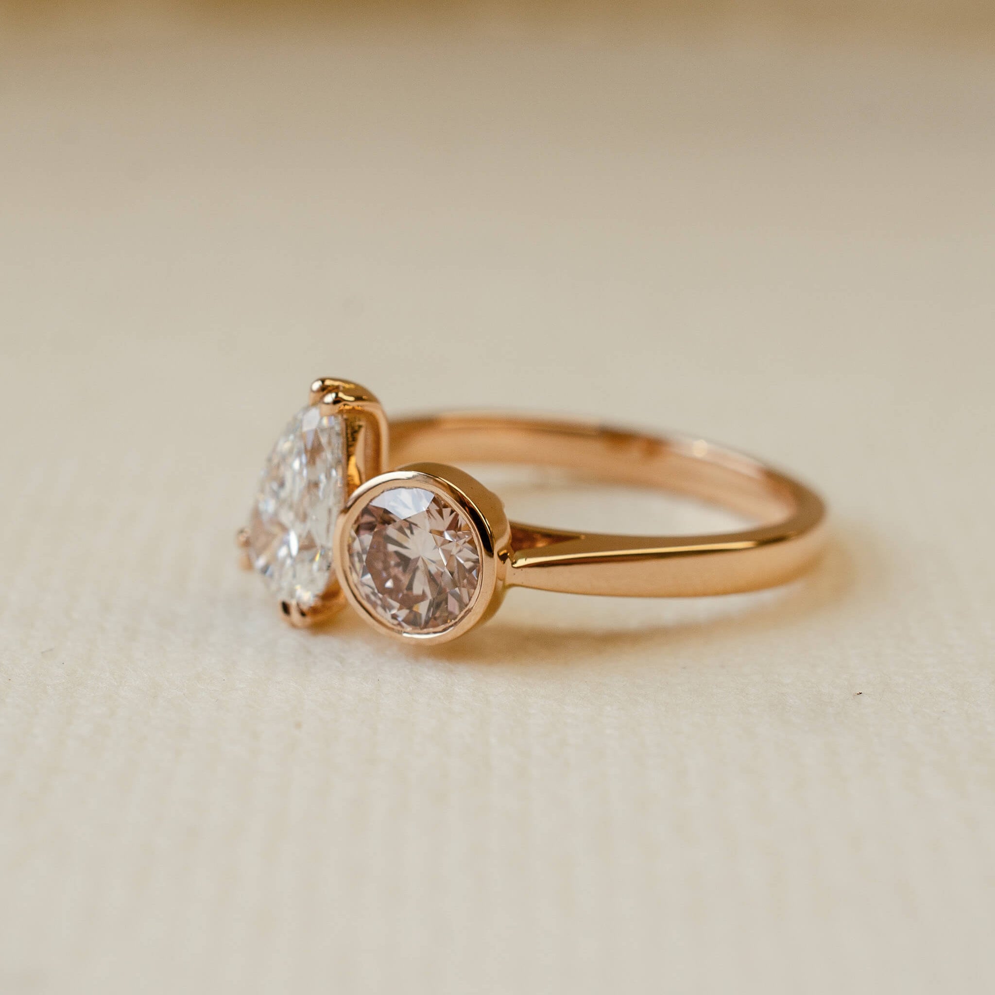 Rose gold ring with two diamonds on a beige background