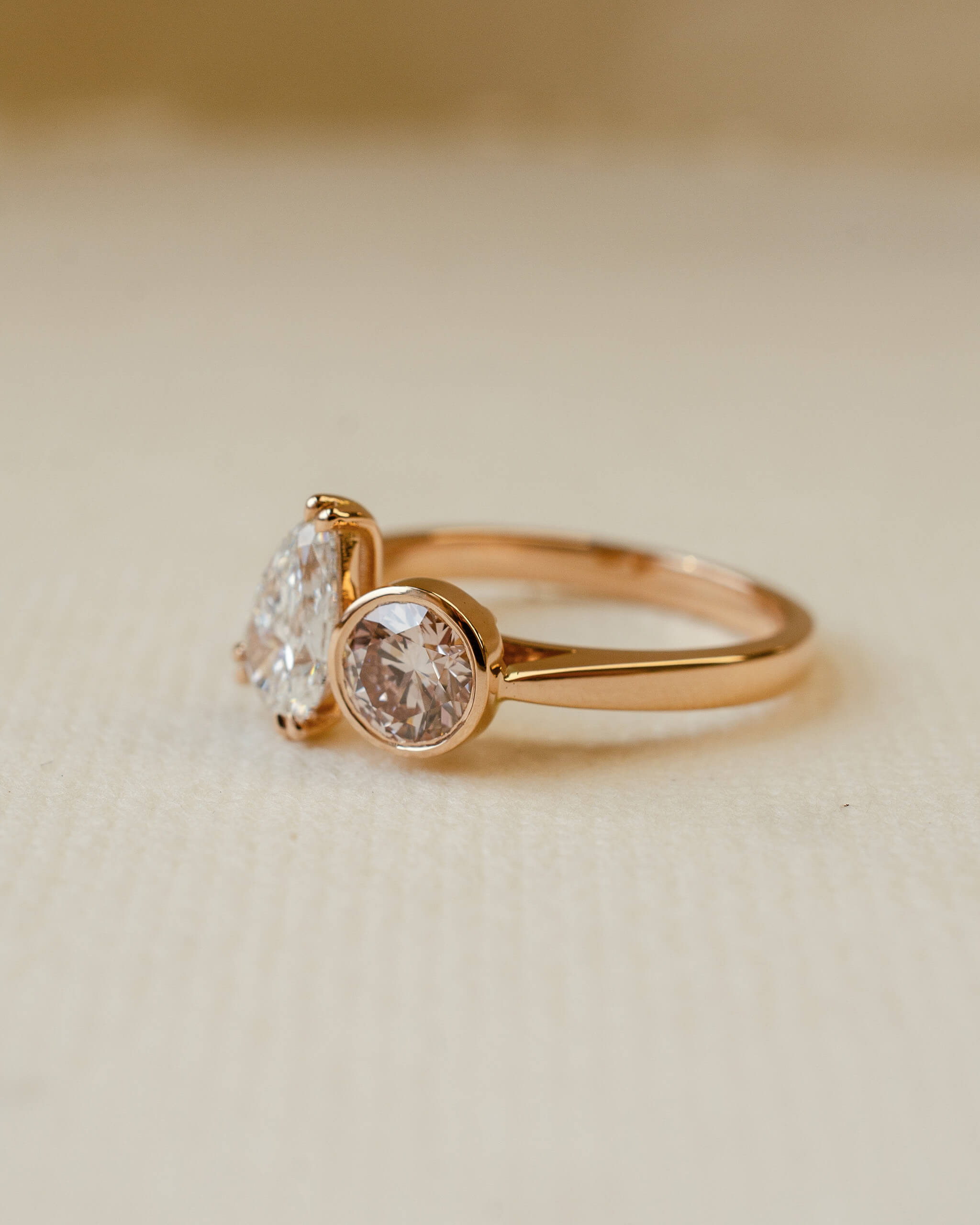 Rose gold ring with two diamonds on a beige background