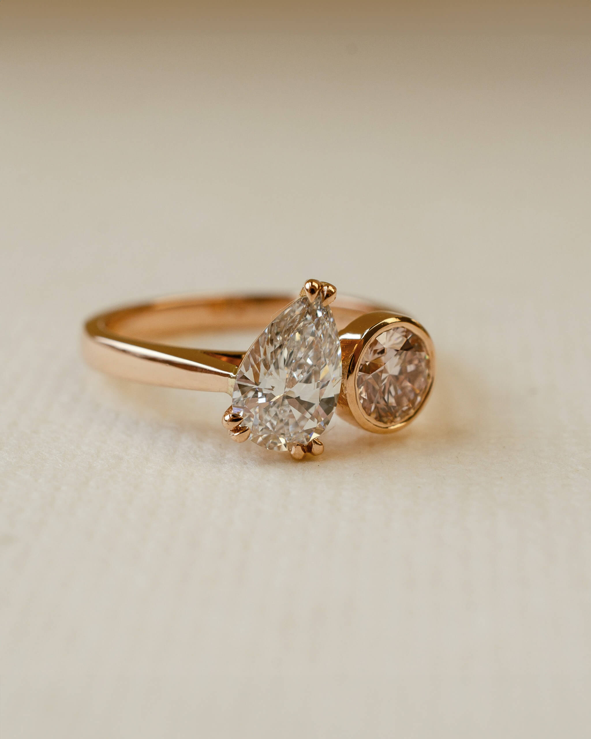 Rose gold ring with two diamonds on a beige background