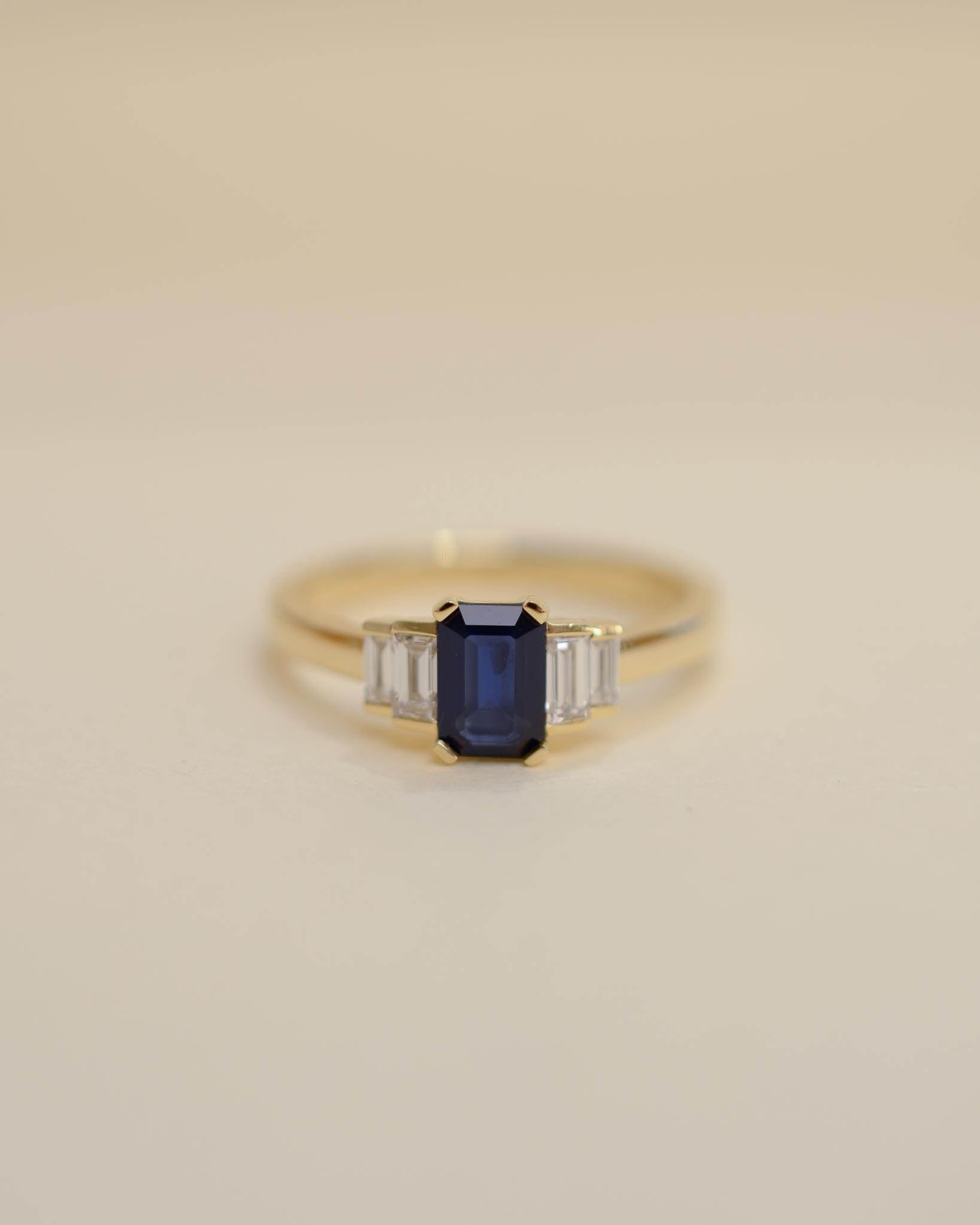 Yellow gold Art Deco style engagement ring set with an emerald cut blue sapphire and baguette cut diamond side stones.