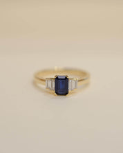 Yellow gold Art Deco style engagement ring set with an emerald cut blue sapphire and baguette cut diamond side stones.