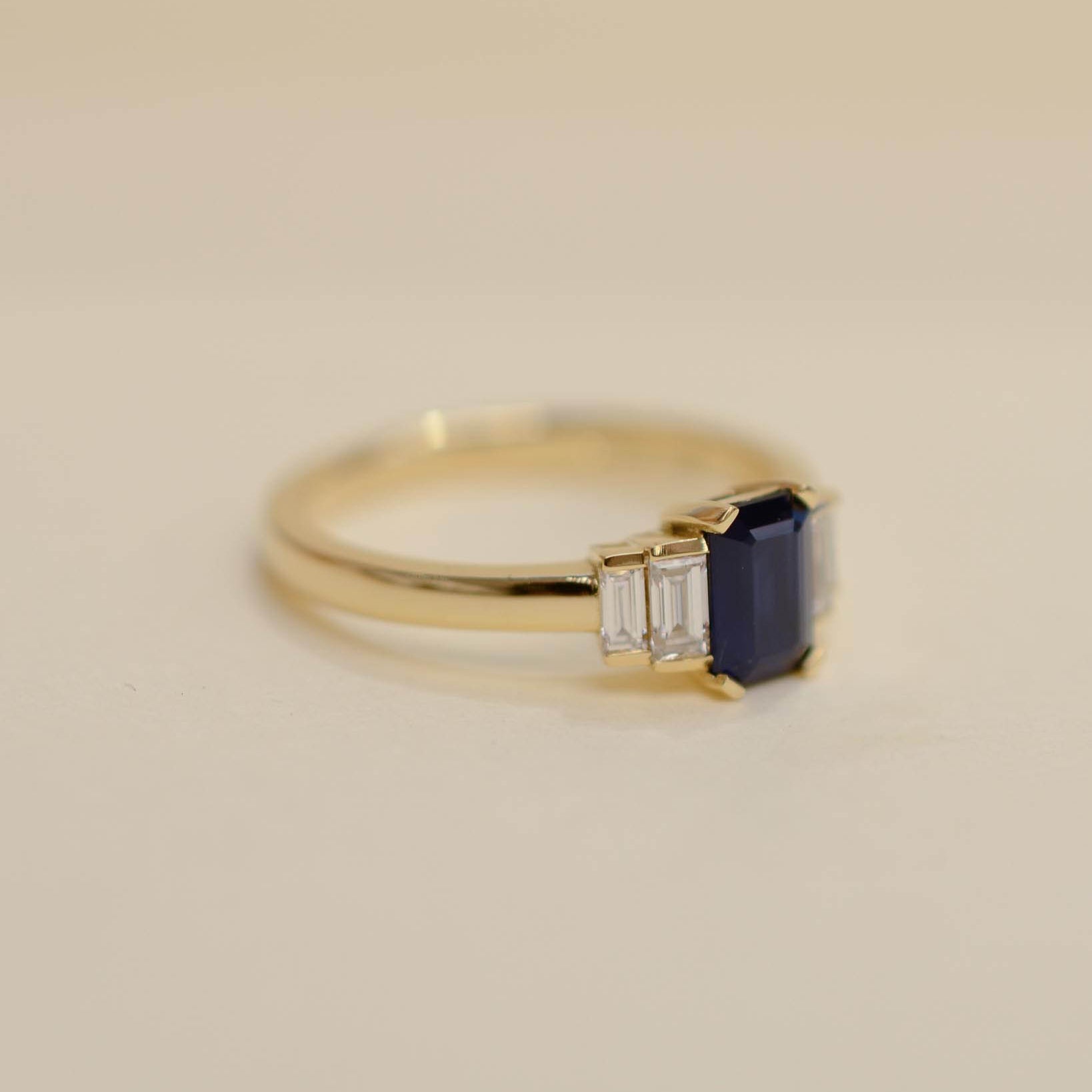 Yellow gold Art Deco style engagement ring set with an emerald cut blue sapphire and baguette cut diamond side stones.