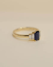 Yellow gold Art Deco style engagement ring set with an emerald cut blue sapphire and baguette cut diamond side stones.