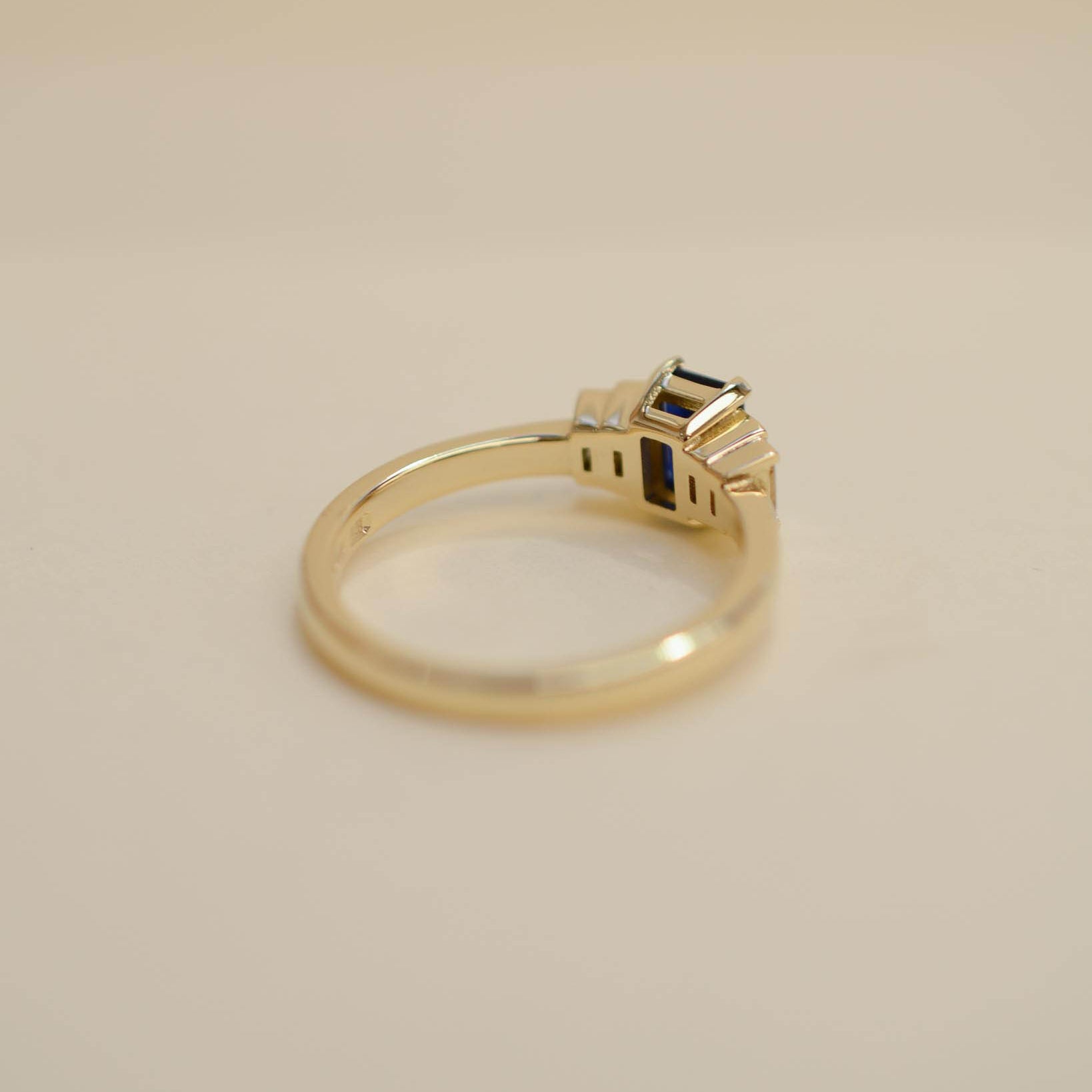 Yellow gold Art Deco style engagement ring set with an emerald cut blue sapphire and baguette cut diamond side stones.