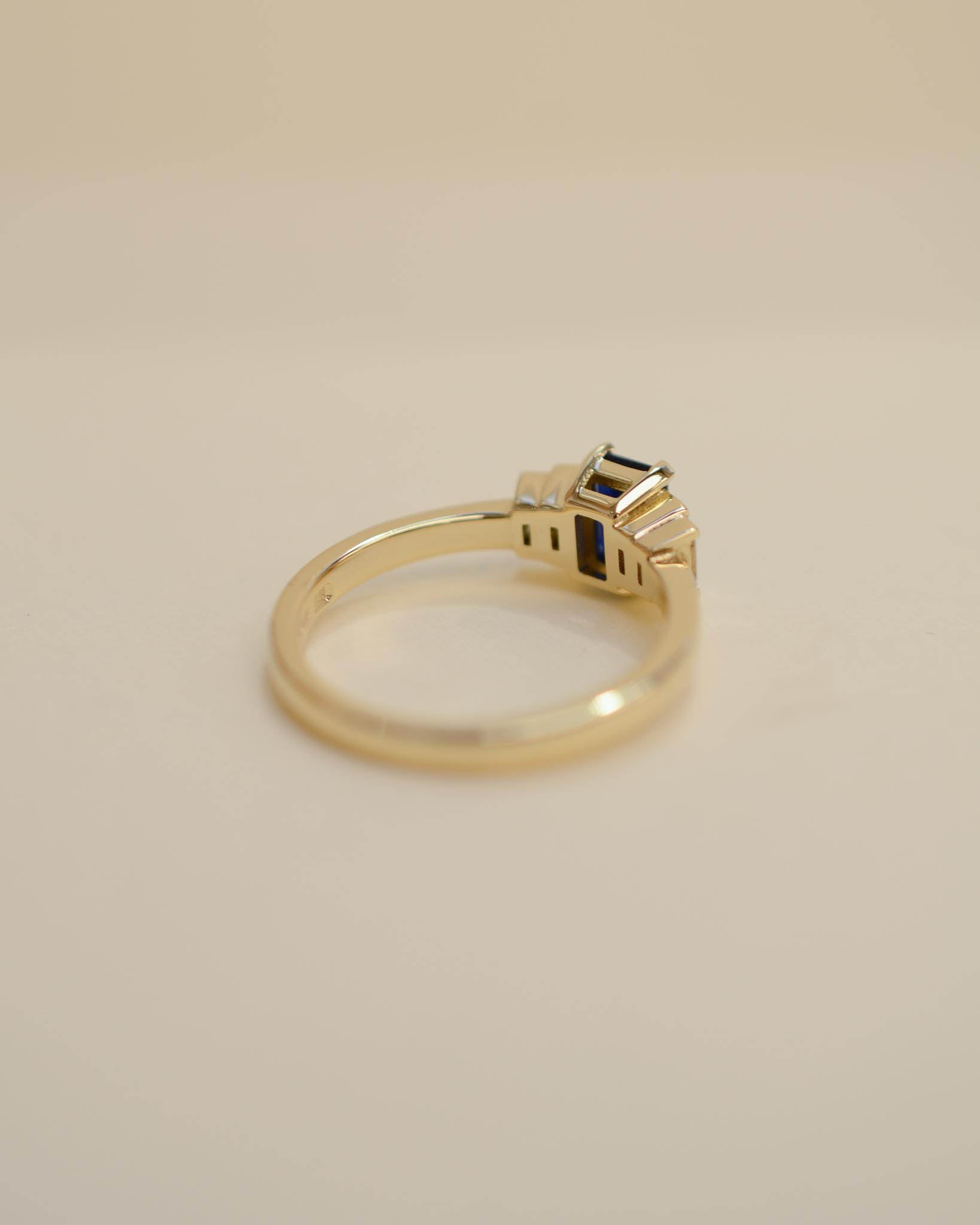 Yellow gold Art Deco style engagement ring set with an emerald cut blue sapphire and baguette cut diamond side stones.
