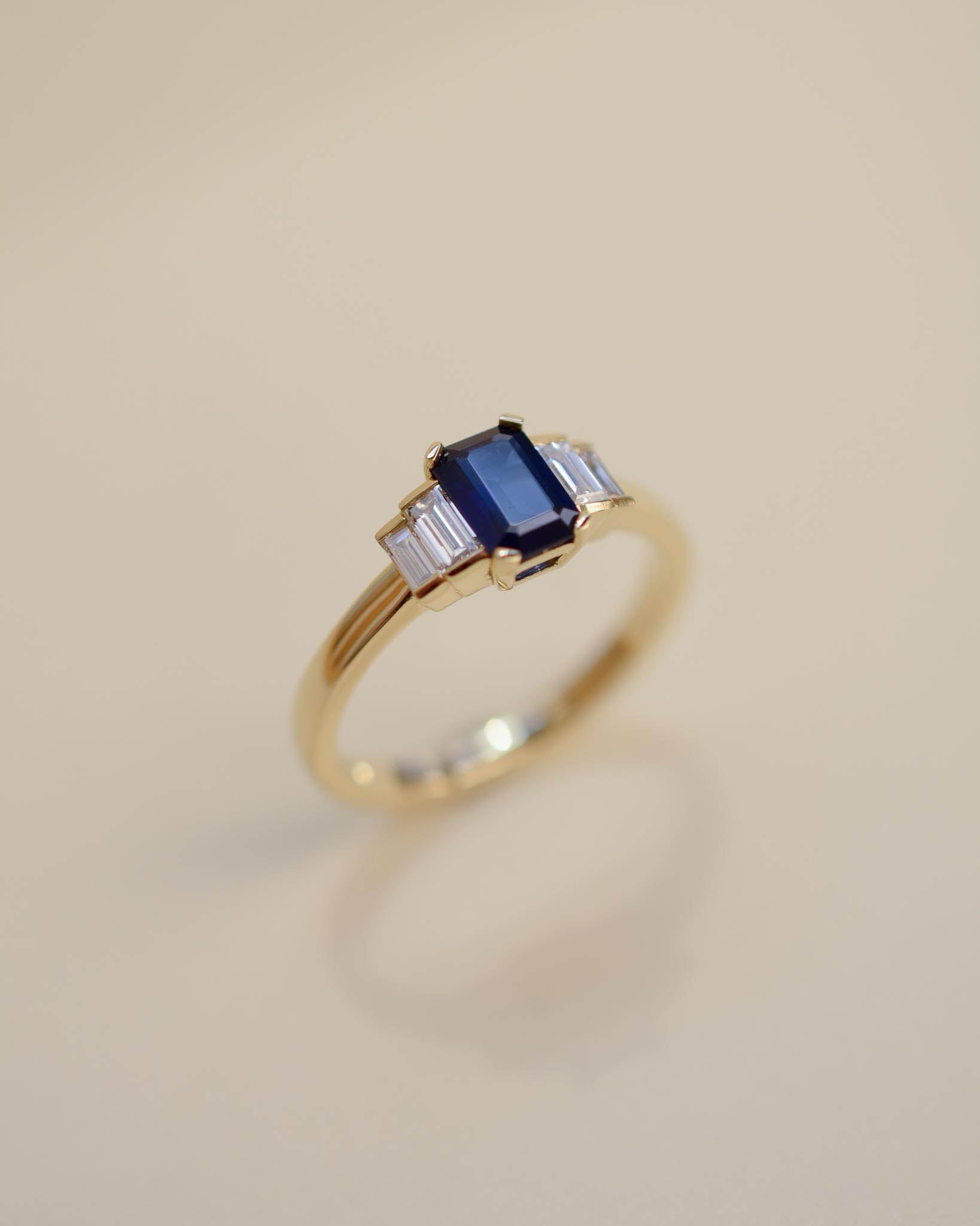 Yellow gold Art Deco style engagement ring set with an emerald cut blue sapphire and baguette cut diamond side stones.