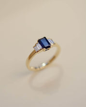 Yellow gold Art Deco style engagement ring set with an emerald cut blue sapphire and baguette cut diamond side stones.