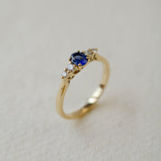 Gold ring with a blue gemstone and smaller diamonds on a light background