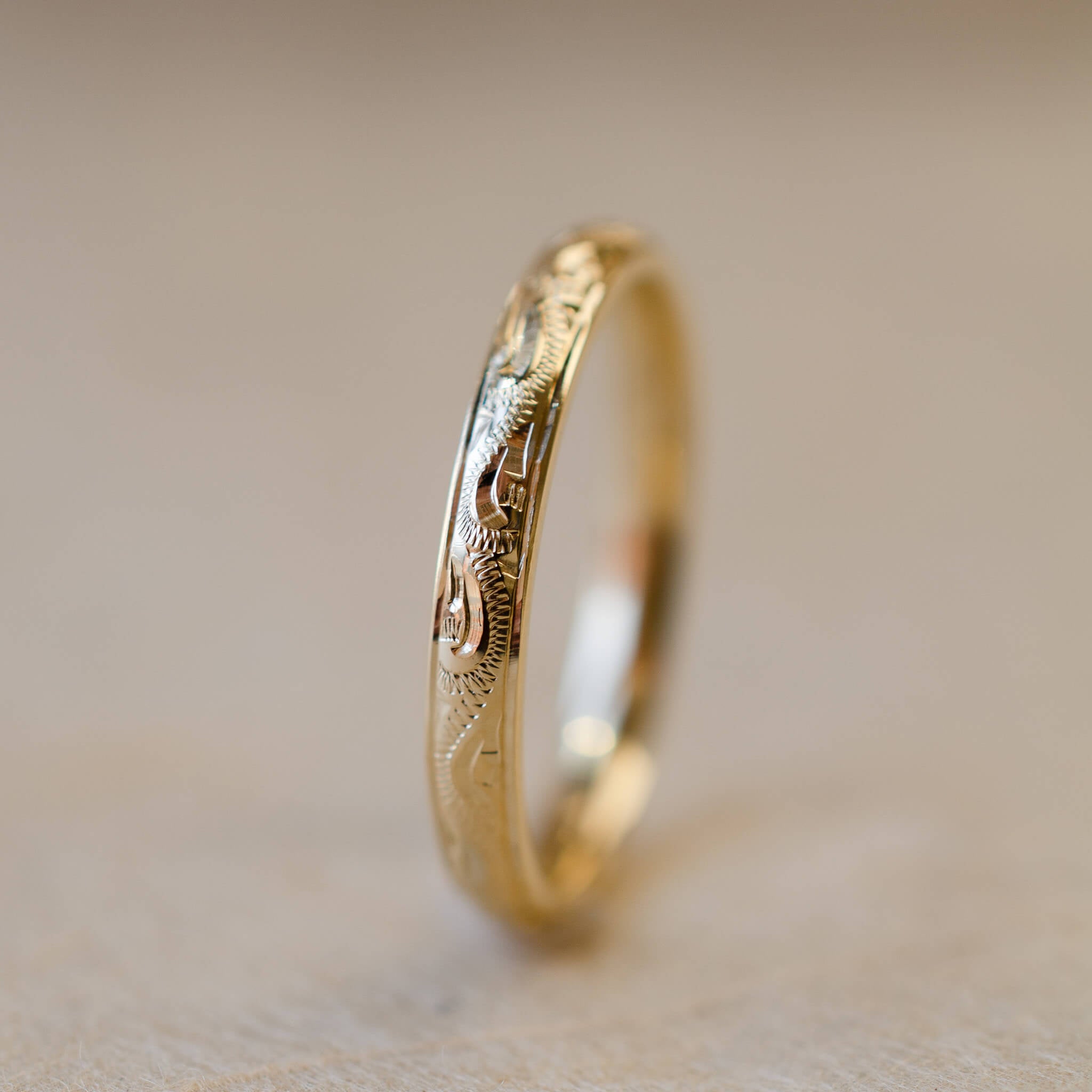 Gold ring with hand engraved design on a beige background