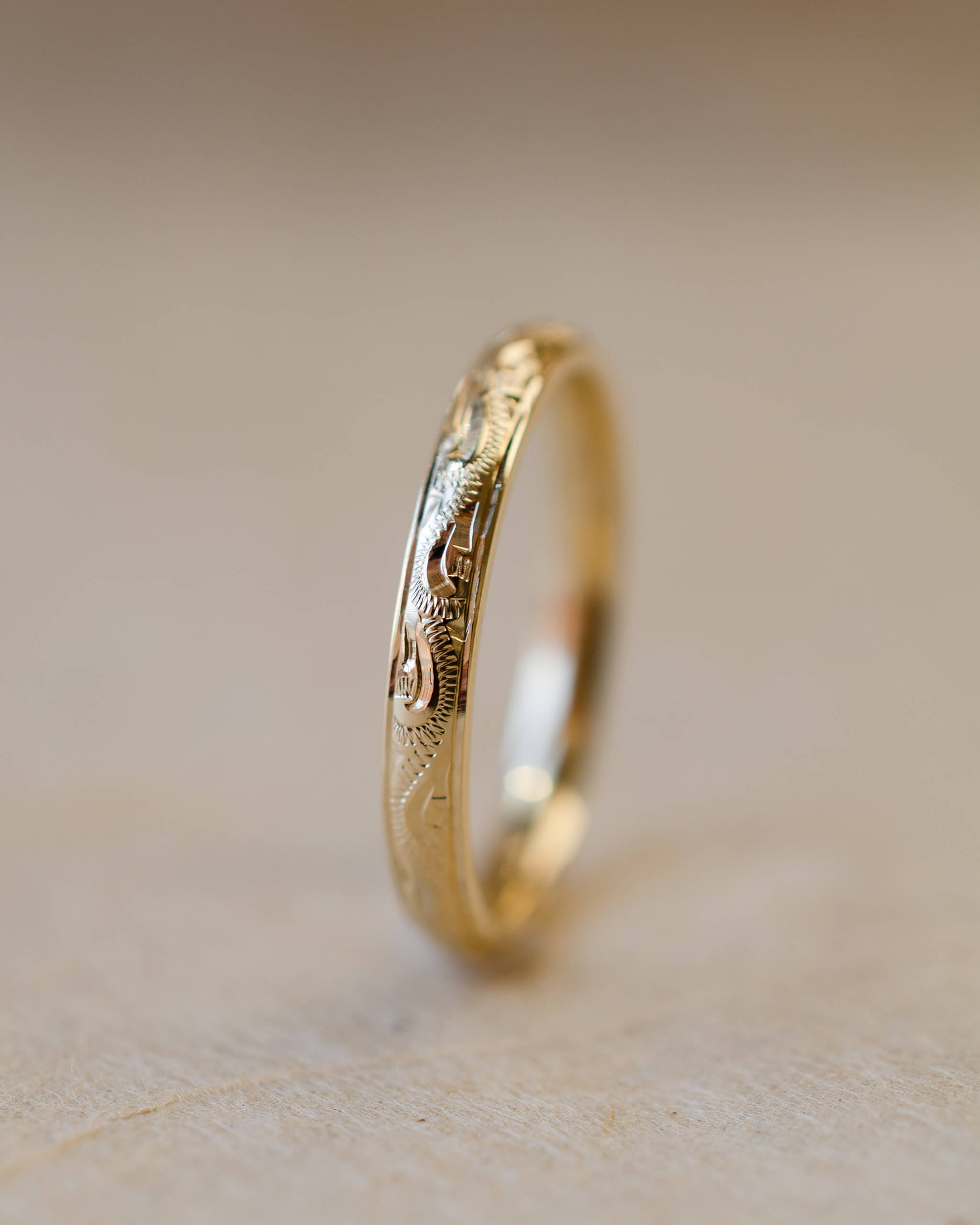 Gold ring with hand engraved design on a beige background