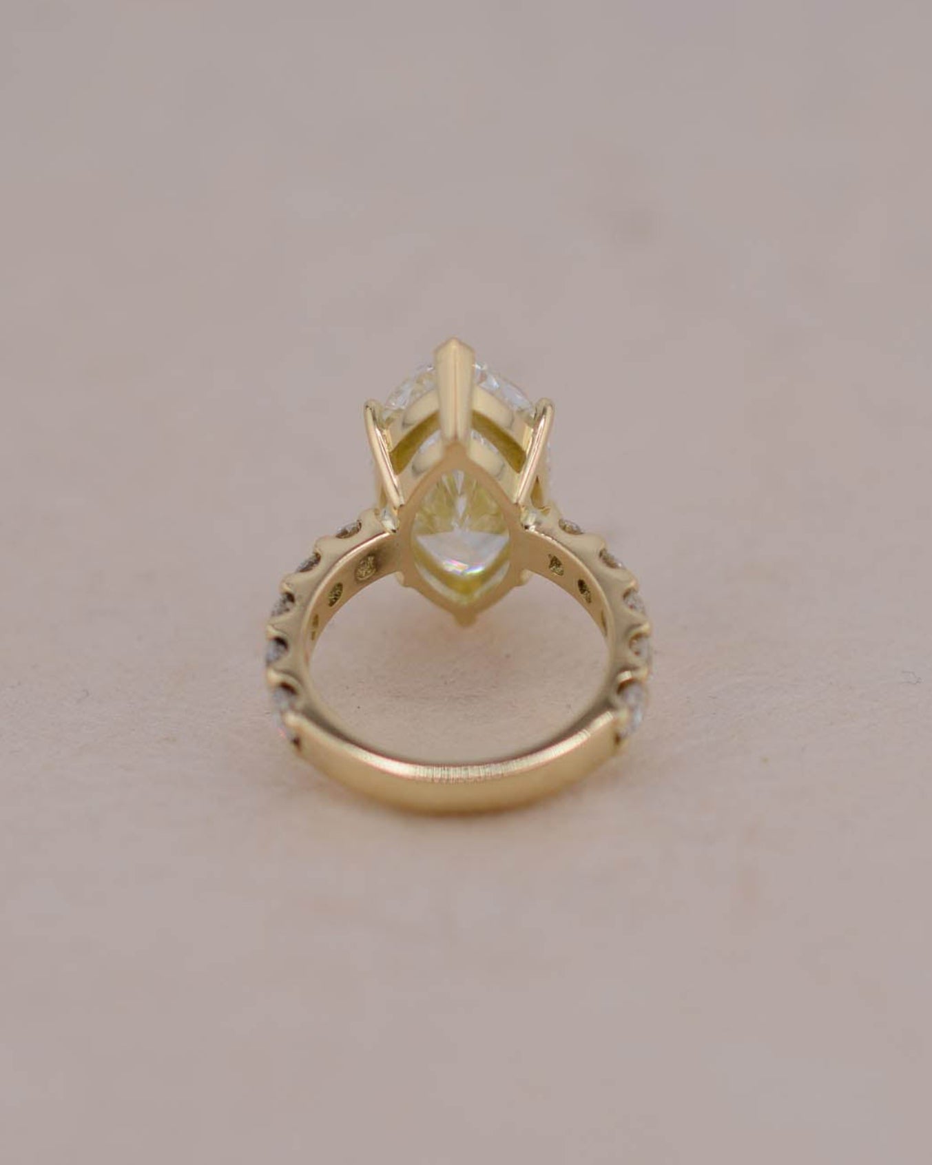 A yellow gold ring featuring a central marquise-cut white diamond in a prong setting, with a decorative openwork band, shown on a plain light beige background.