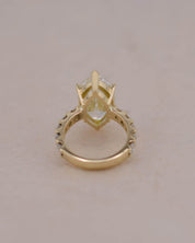 A yellow gold ring featuring a central marquise-cut white diamond in a prong setting, with a decorative openwork band, shown on a plain light beige background.