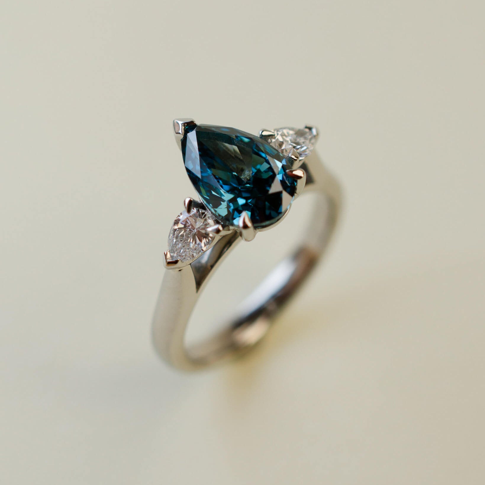 trilogy ring with teal pear cut diamond centre stone and white pear diamond side stones