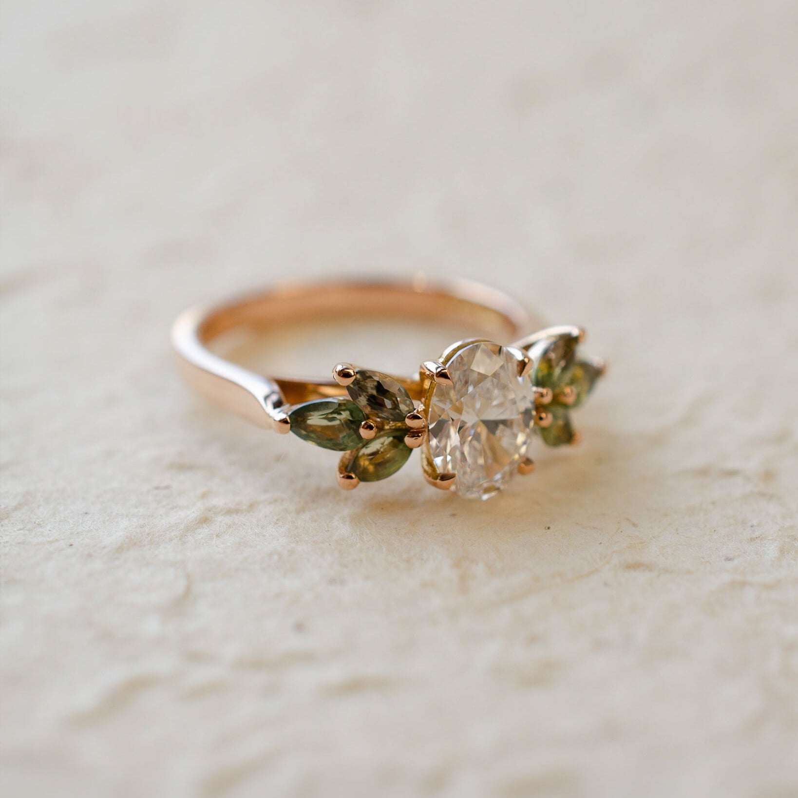 Rose gold engagement ring with white oval diamond centre and marquise cut green sapphires