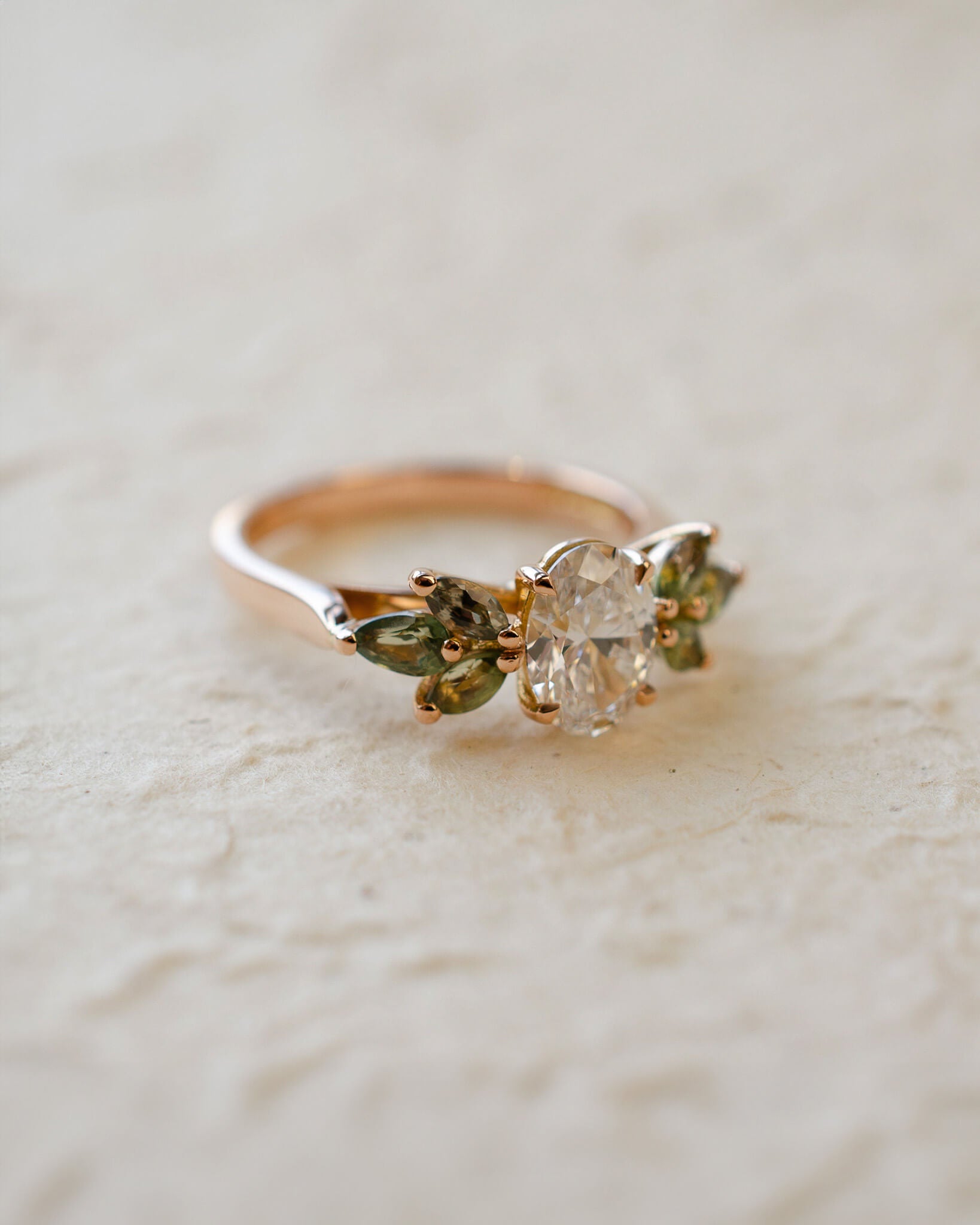 Rose gold engagement ring with white oval diamond centre and marquise cut green sapphires