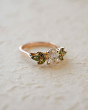 Rose gold engagement ring with white oval diamond centre and marquise cut green sapphires
