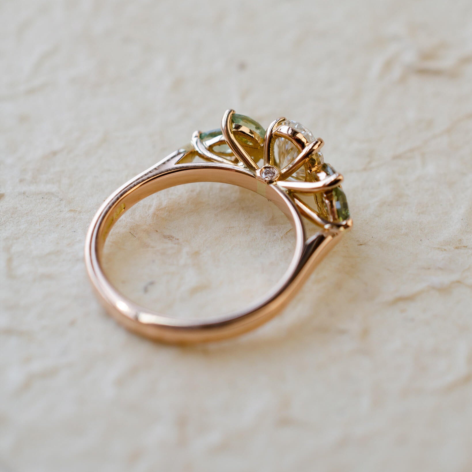 Rose gold engagement ring with white oval diamond centre and marquise cut green sapphires