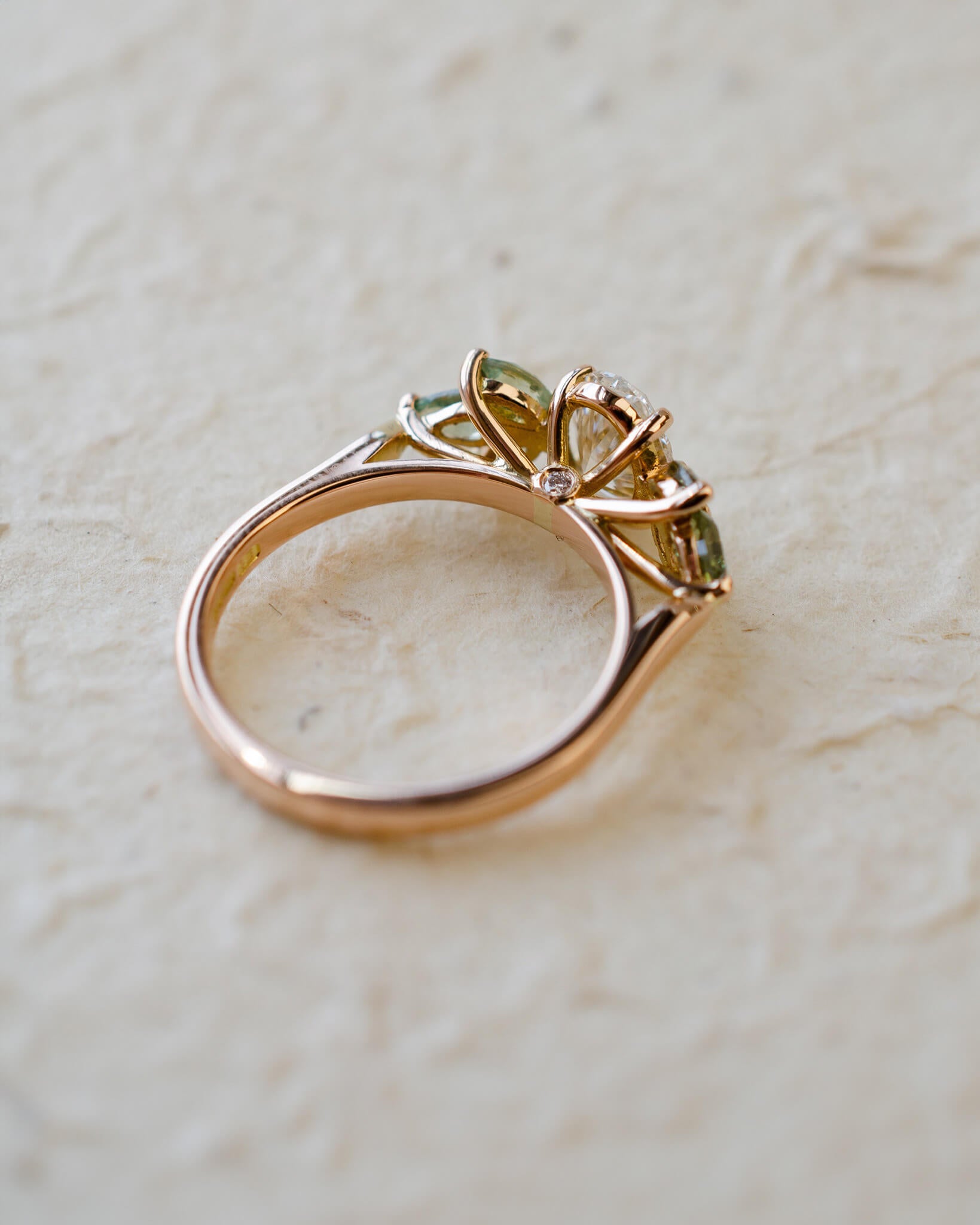 Rose gold engagement ring with white oval diamond centre and marquise cut green sapphires