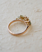 Rose gold engagement ring with white oval diamond centre and marquise cut green sapphires