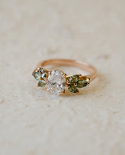 Rose gold engagement ring with white oval diamond centre and marquise cut green sapphires