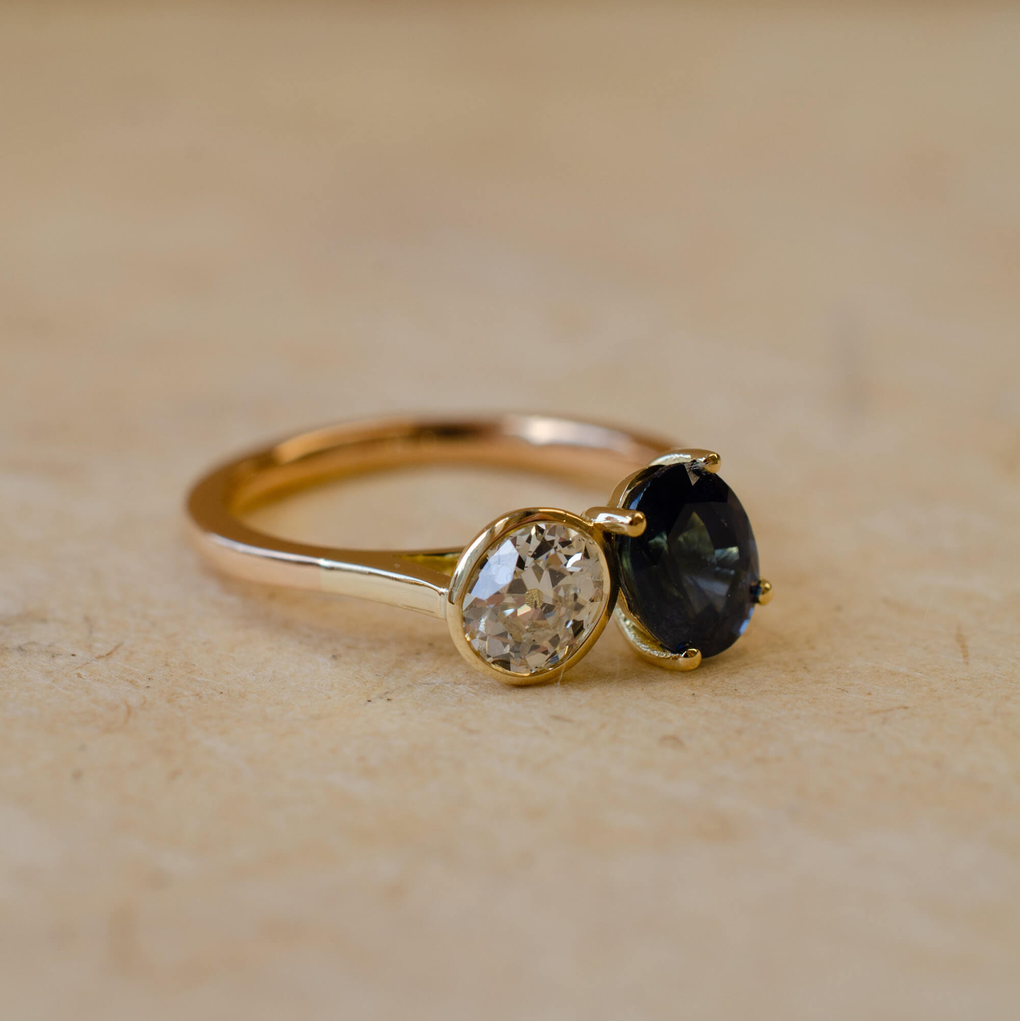 Gold ring with two gemstones on a beige surface
