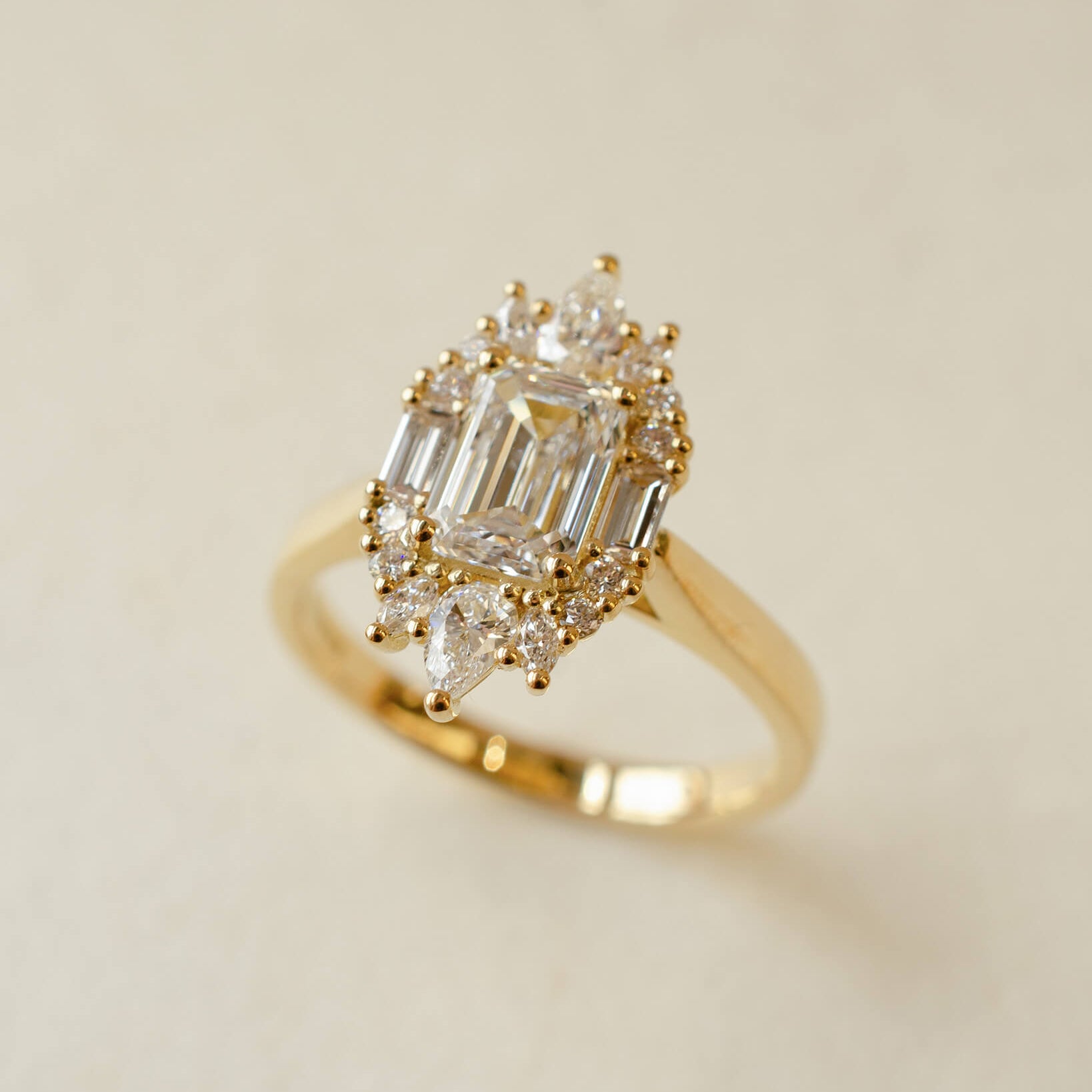 Gold ring with emerald-cut and pear-shaped diamonds on a beige background